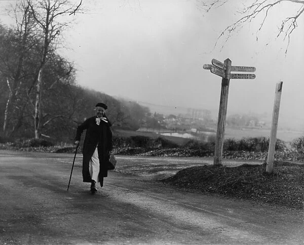 Elderly nurse walking down a country lane past a crossroad sign, c1930