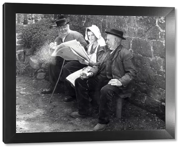 Three people reading a newspaper in a farmyard, 1930s