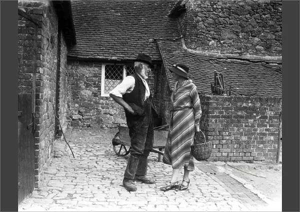 Lady and farm worker talking in farmyard, September 1933