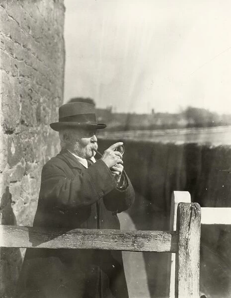 Gentleman lighting his pipe with a magnifying glass, March 1933