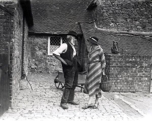 Lady and farm worker talking in farmyard, September 1933