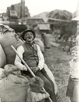 Old character with young boys, threshing machinery in the background, 1932