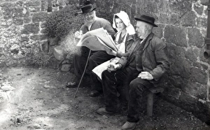 Three people reading a newspaper in a farmyard, 1930s